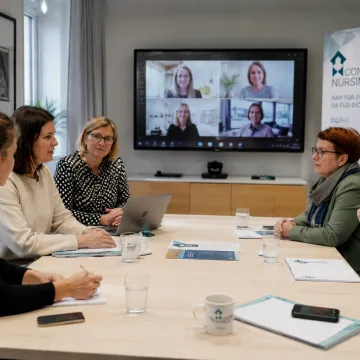 Fünf Frauen sitzen an einem Tisch und tauschen sich mit vier virtuell zugeschaltenen Frauen aus