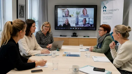 Vernetzungstreffen. Fotocredit: KI-generiert mit ChatGPT Fünf Frauen sitzen an einem Tisch und tauschen sich mit vier virtuell zugeschaltenen Frauen aus